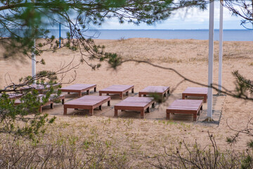 Wooden sun loungers on the beach with pine spruce trees, peeping out of the woods behind the beach