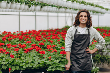 Happy worker, wearing apron, growing flowers in a greenhouse of a flower shop.