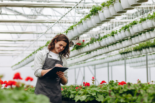 Close-up. Young handsome male florist watching on flowers and making notes.