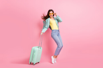 Photo portrait full body view of woman standing on tip toes with teal suitcase isolated on pastel pink colored background