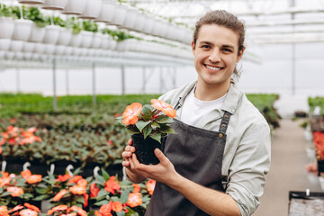Portrait of a young man florist that cares for the flowers in the greenhouse.