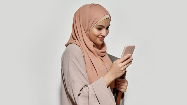 Cheerful arabian girl student in hijab using smartphone