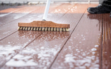 Detail of a scrubbing brush during spring cleaning on a wooden terrace with soap and splashes of...