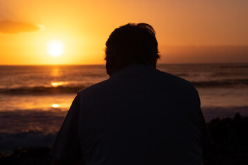 Senior man silhouette relaxing looking at the horizon the magnificent orange sunset at sea.