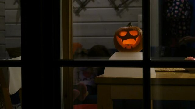 View through window at home. Halloween pumpkin at window. Children playing at home on halloween night. 
