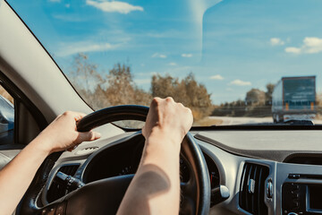 Female hands confidently hold steering wheel of car while driving on suburban highway with traffic. Overtaking truck on road, inside view of dashboard. Woman driving rental car