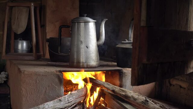 Close up of metal teapot heating water to make organic coffee on the fire in a rustic wood stove. Minas Gerais, Brazil. Concept of, winter, cold, cozy, vintage, morning, coffeemaker, retro. 4K