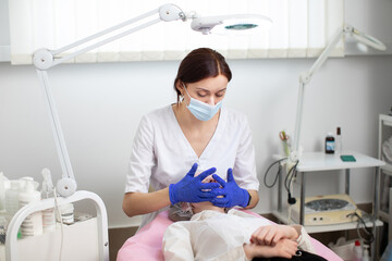 Young female doctor cosmetologist in protective mask and blue rubber gloves makes facial massage and skin treatment for young woman client. Spa face massage in beauty salon, facial beauty treatment