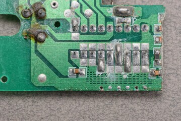 part of a green old plastic microcircuit with lead soldering lies on a gray table