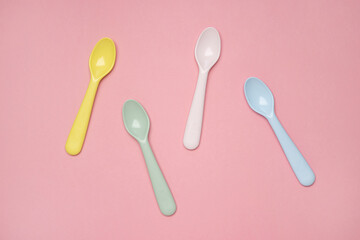 Kid spoons in different colors laid on sweet pink pastel background, a set of colorful spoons,...