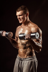 Serious tattoed shirtless athlete lifting metal dumbbells training on dark background