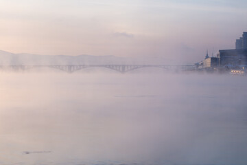 Bridge and fog across the river on the background of a beautiful sunset in winter