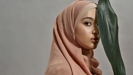 Young arabian woman in hijab next to green leaf