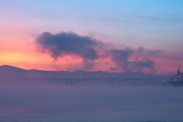 Bridge and fog across the river on the background of a beautiful sunset in winter