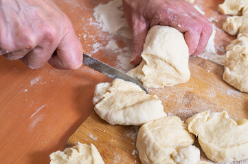 A woman cuts raw dough into portions for baking buns. Homemade buns and pies