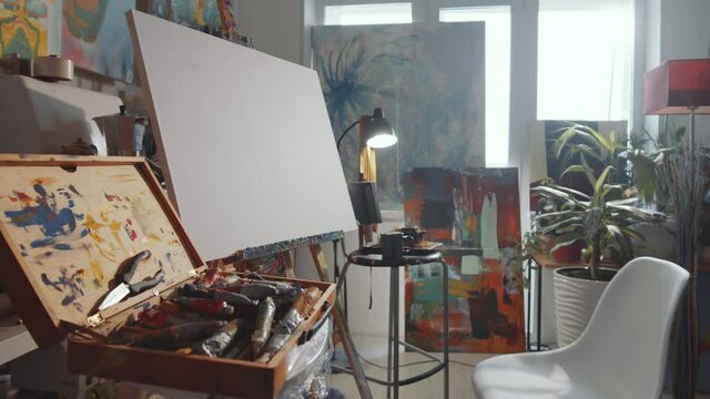 Zoom in shot of blank canvas on easel and case with painting tools in art studio with no people