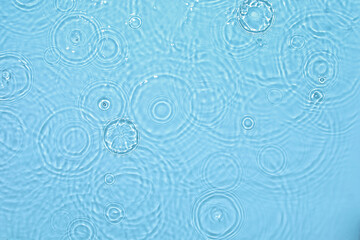 De-focused transparent blue colored clear calm water surface texture with ripples, splashes and bubbles. Trendy abstract nature background. Water waves in sunlight with copy space.