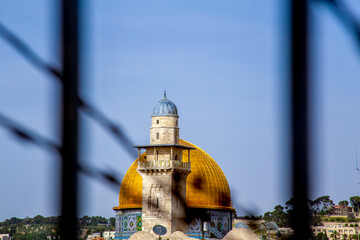 Jerusalem, Israel - 21 april 2021: minaret and dome of rock through barbed wire on a sunny day, selective focus