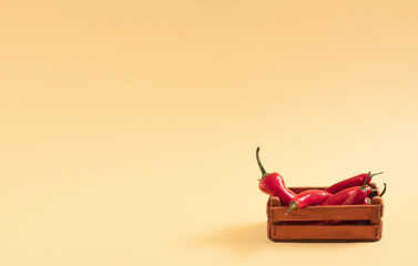 Red chili peppeprs in a wooden box on a pastel background, composition with copy space