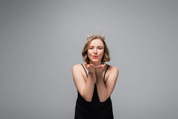 Fototapeta premium happy plus size woman in black slip dress and crown sending air kiss isolated on grey