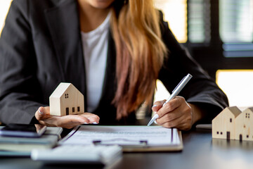 Close up wooden toy house with business woman signs a purchase contract or mortgage for a home,...
