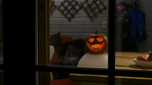 View through window at home. Halloween pumpkin at window. Children playing at home on halloween night. 