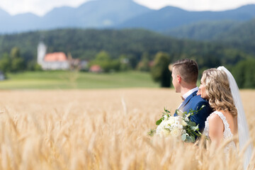 Naklejka na ściany i meble Bride hugs groom tenderly in wheat field somewhere in Slovenian countryside.