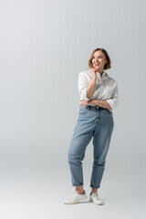 full length of happy overweight woman in jeans posing on grey