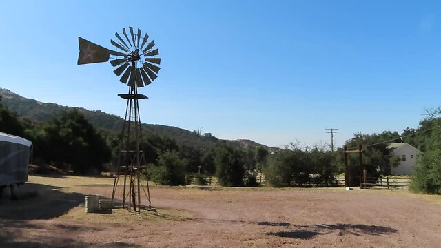 Farm Windmill Rotating in the Wind Near a Dirt Parking Lot