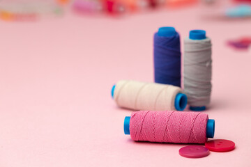 Multicolored thread spools and buttons on pink background