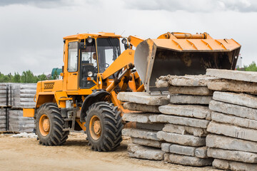 Bulldozer or excavator industrial heavy machine at a construction site unloads old concrete stone slabs material