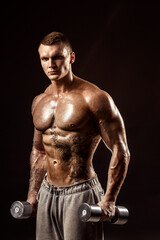 Fototapeta na wymiar Serious tattoed shirtless athlete lifting metal dumbbells training on dark background