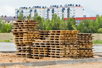 Pile of old wooden pallets storage timber materials at a construction site on the background of modern urban houses