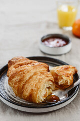 Breakfast with croissant, jam and hot chocolate, juice and tangerine on greige linen tablecloth. Selective focus