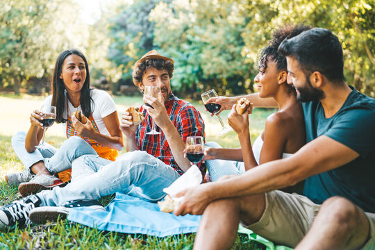 Interracial young people meeting having a picnic eating sandwiches and drinking wine in the nature.