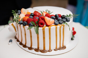 A beautiful wedding cake decorated with fruits, raspberries, strawberries and blueberries, watered with caramel. Confectionery on the table. Holiday concept.