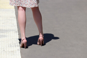Slim female legs on high heels, woman in summer dress and high-heeled shoes standing on a street in...