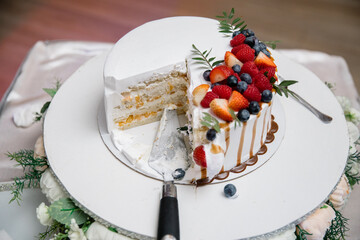 A cut piece of wedding cake, garnished with fruits, raspberries, strawberries and blueberries, watered with caramel. Close-up. Top view. Holiday concept.