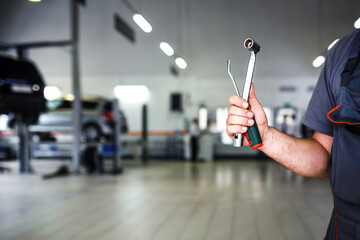 The hand of a car repairman with keys and a special tool on the background of the service area. A mechanic in a car service station in uniform. Copy space