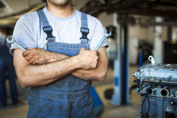 The hand of a car repairman with keys and a special tool on the background of the service area. A...