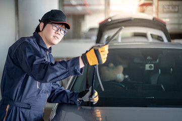 Young Asian auto mechanic checking windshield wiper in auto service garage. Mechanical maintenance engineer working in automotive industry. Automobile servicing and repair - obrazy, fototapety, plakaty