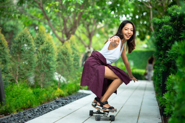 Asian young women surf skate or skates board outdoors on beautiful summer day. Happy young women play surf skate at park.