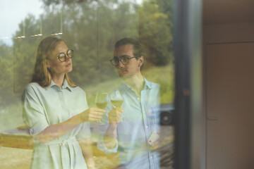 Portrait through a glass window of successful couple celebrating on the kitchen