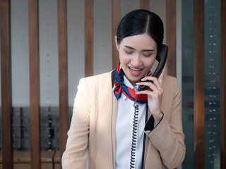 A confident, beautiful woman receptionist talking on the phone with a smiling face at the reception counter inside the hotel.