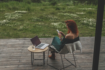 Back view of freelancer girl with smartphone and laptop working on vacation