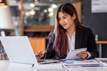 Portrait of Business young woman working on laptop computer doing finances,accounting analysis,report,data and pointing graph at the office.