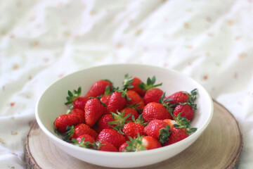Bowl of fresh strawberries and wooden tray on a bed. Selective focus.