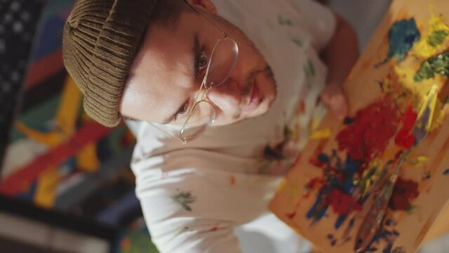 Top down spinning camera shot of young male painter holding wooden palette and painting picture in art studio