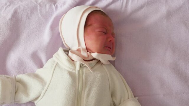 Baby girl is writhe, shake hands and squeeze eyes, call mother. Portrait shot of infant child with original sound. Very young human have red and peeling first skin