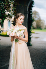 Fototapeta na wymiar Bride in a beautiful dress with bare shoulders holds a bouquet of pink flowers against the backdrop of an arch entwined with greenery. Lake Como, Italy